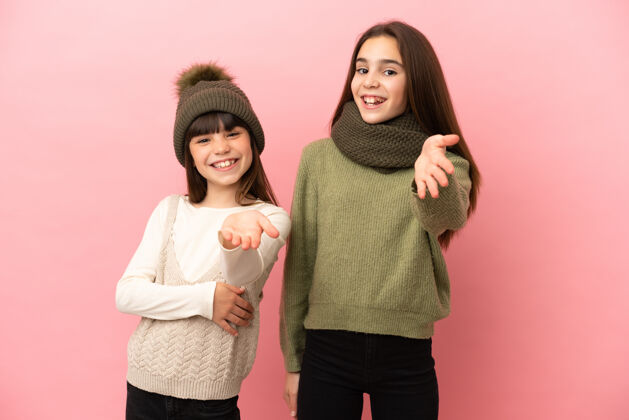 欢迎小姐妹们穿着冬装孤立地站在粉色的背景上握手表示成交不错温暖童年握手