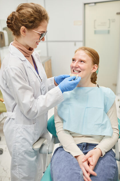 牙医牙医和病人一起工作他们正在为新牙选择植入物助手实验服医院