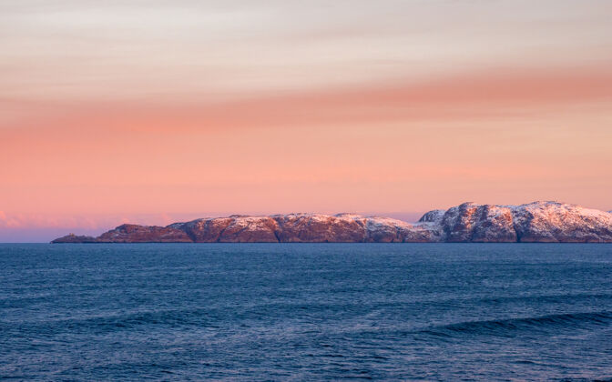 极地北冰洋上美丽的粉红色日落半岛上有白雪覆盖的小山地平线.海极简主义景观.全景查看岛屿凉爽水平