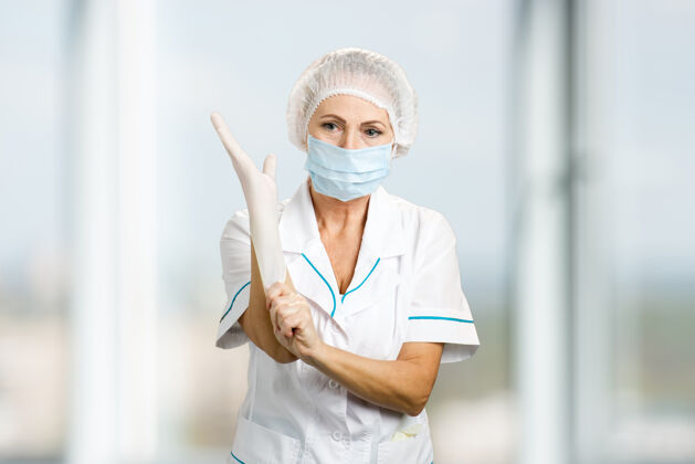 信心女外科医生戴上手套女医生戴上防护口罩和帽子戴上白色防护手套 迷糊了制服帽子医生