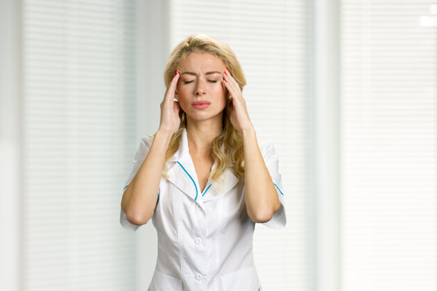 诊所头痛剧烈的年轻护士解开年轻护士或女医生的手 闭上眼睛放在颧骨上工作疼痛治疗