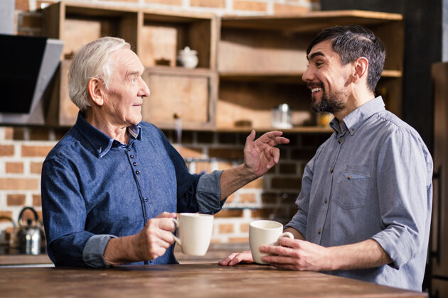 退休快乐微笑的老人在厨房休息时和儿子说话咖啡老年人关心