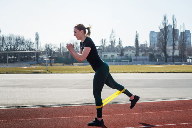 健康年轻的运动型女子在红色跑道上用健身橡皮筋训练腿部女人强壮肌肉