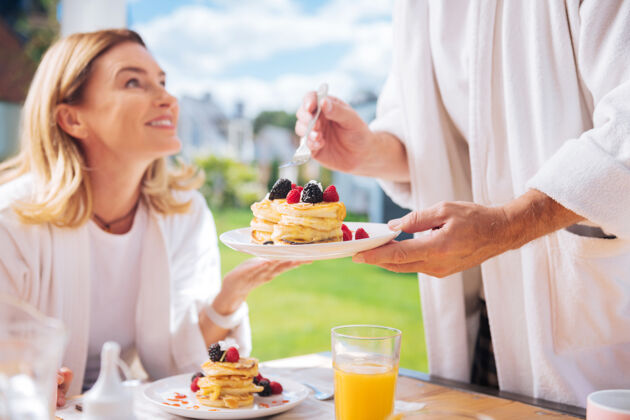 丈夫美味的早餐有爱心的丈夫提供美味的热煎饼和新鲜的橙汁作为早餐露台浴袍气氛