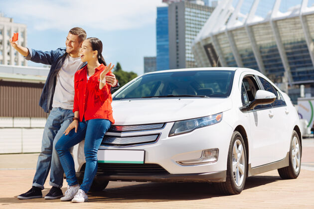 当代新买的快乐的夫妇站在他们的车旁边自拍保护宽容移动