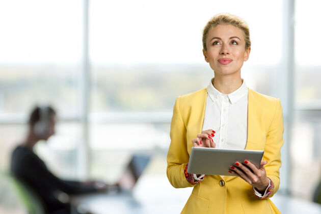 欧洲体贴的商务女士拿着数字平板电脑漂亮的商务女士站在办公楼的窗户前 一边用数字平板电脑一边往上看成人商务女性