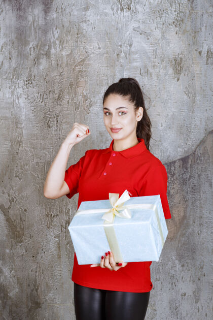 成人一个十几岁的女孩手里拿着一个用白丝带包着的蓝色礼盒 上面写着“享受”的手势姿势服装快乐