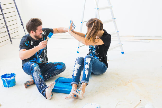 装修装修重新装修和内饰概念年轻夫妇坐在白色地板上倒油漆室内设备胶水