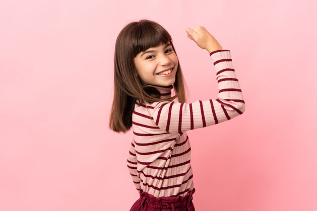 自信小女孩孤零零地站在粉红色的墙上做着坚强的手势墙乐趣人