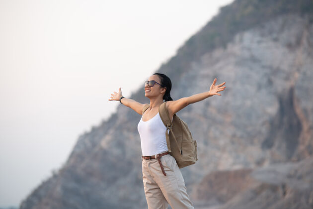 徒步旅行者徒步旅行时 一位妇女在山顶举手 站在岩石山脊上的电线杆眺望山谷和山峰活动徒步旅行乡村
