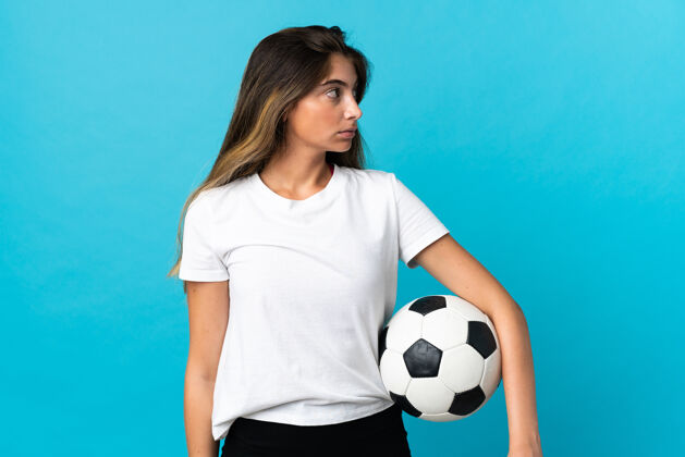 运动装年轻的白种女人拿着足球被隔离在蓝色的墙上多彩足球训练