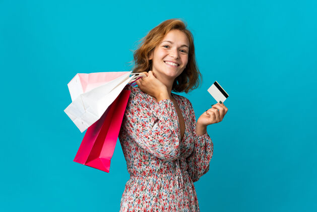 购买格鲁吉亚年轻女子 手拿购物袋 蓝色背景 手拿购物袋和信用卡积极支付借记