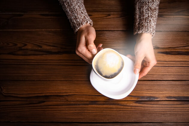 泡沫木制背景上的女性手和咖啡咖啡人杯子