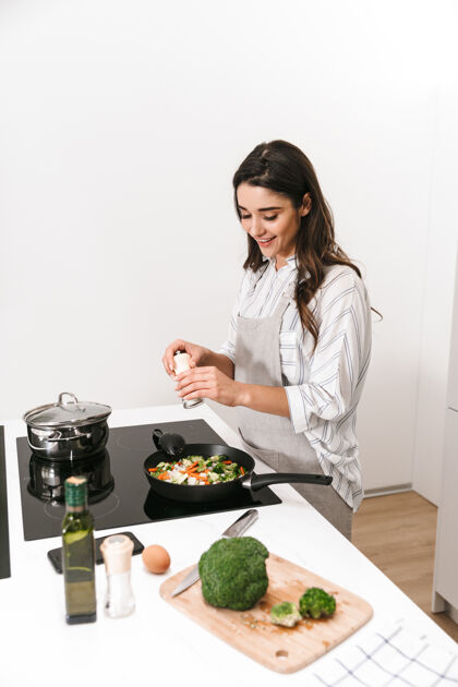 人漂亮的年轻女子在厨房用煎锅做健康的晚餐蔬菜食物站立