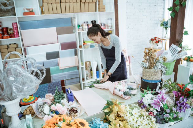 花束在花店工作的年轻女花匠在桌子工作区定做法兰绒花女性开花束