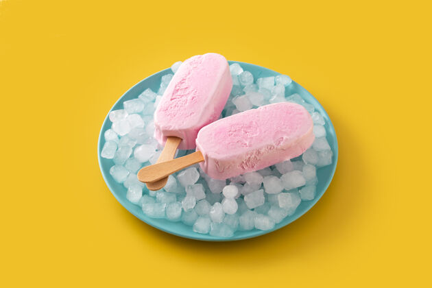 立方体草莓冰棒和碎冰放在黄色桌子上的蓝色盘子里零食压碎棒棒糖