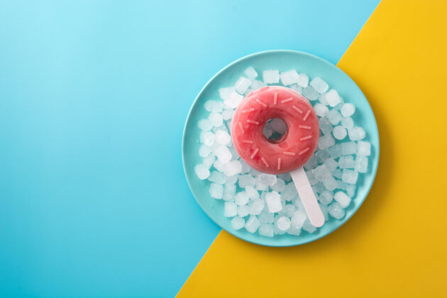 圆形草莓甜甜圈冰棒和碎冰放在黄色和蓝色的桌子上甜点冰棒棒糖
