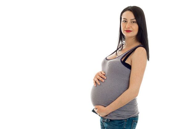漂亮年轻的黑发孕妇在白色的墙壁上摆出孤立的姿势人怀孕肚子