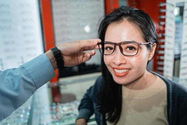 女性一名员工的手正在帮助戴上一副眼镜 这副眼镜是一位做过眼科检查的女士在眼科诊所挑选的检查女人镜片