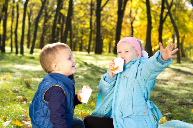 一起两个可爱的小孩坐在五颜六色的秋天林地的地上 享受着清爽的饮料玩耍森林孩子