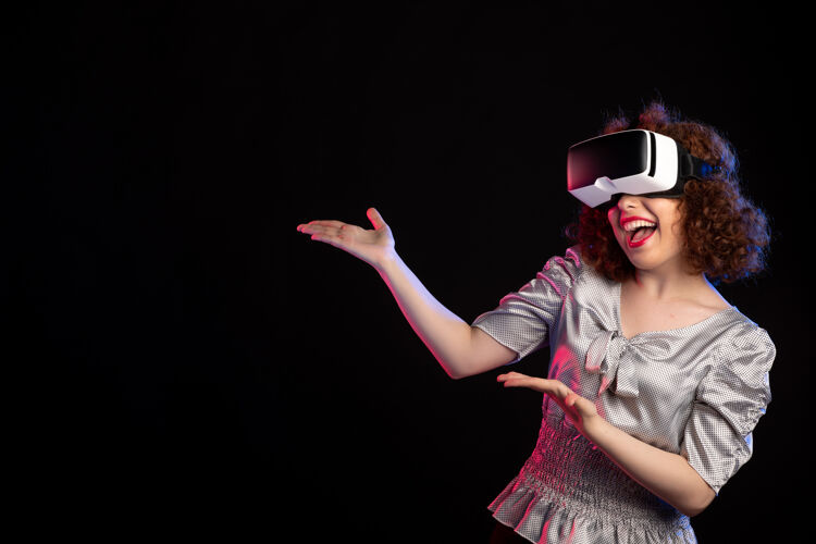 虚拟戴着虚拟现实耳机的年轻女性在黑暗的视觉技术游戏中表演年轻女性穿着