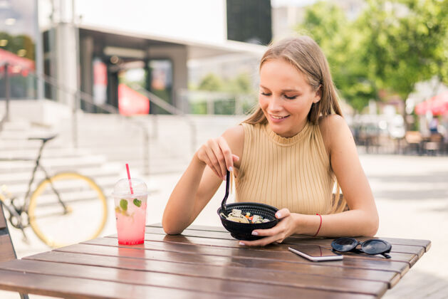 夏天在街边咖啡馆吃沙拉的年轻漂亮女人的特写镜头坐着街道美味