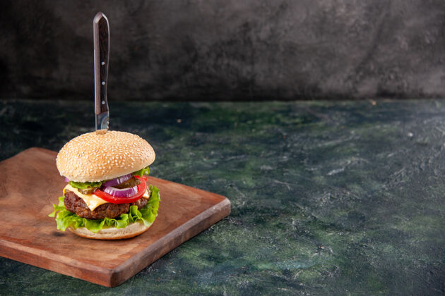汉堡包刀在美味的肉三明治上的木质砧板上 在右侧的隔离黑暗表面上有自由空间板刀壁板