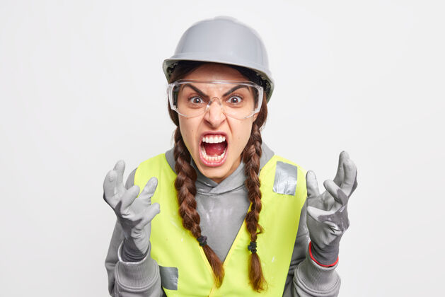 尖叫愤怒的女建筑工人愤怒的手势大声尖叫被犯了大错误的伙伴惹恼戴安全帽手套安全眼镜制服恼怒服务员工