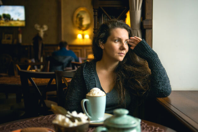 短信漂亮的棕色头发的年轻女孩坐在咖啡馆里喝着卡布奇诺女人头发杯子
