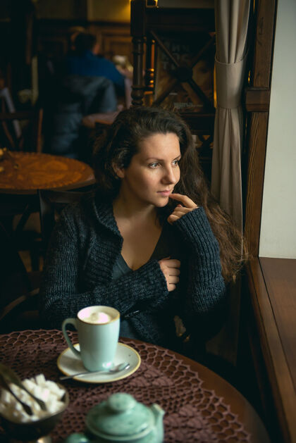 茶漂亮的棕色头发的年轻女孩坐在咖啡馆里喝着卡布奇诺女人黑发咖啡馆