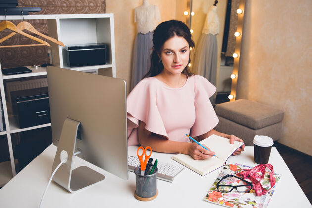 职业穿着粉色豪华连衣裙的年轻时尚女士在办公室用电脑工作人科技衣服