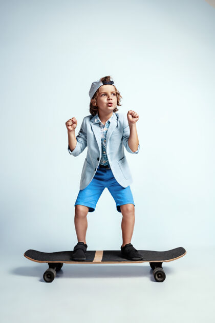 牛仔裤在白色的工作室墙上 穿着休闲服的漂亮男孩在滑板上滑板男性小