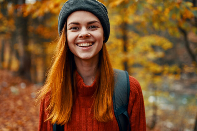 公园一个穿着帽子毛衣 背着背包的美丽女人的肖像在秋天的森林里游客女性摄影