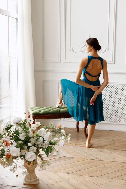 优雅穿着蓝色连衣裙的优雅迷人的女孩背对着窗户站着女性人芭蕾舞