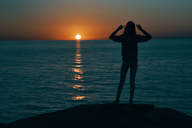 女人日落时分 一个女人在海边做手势 双手向后看平静轮廓阳光