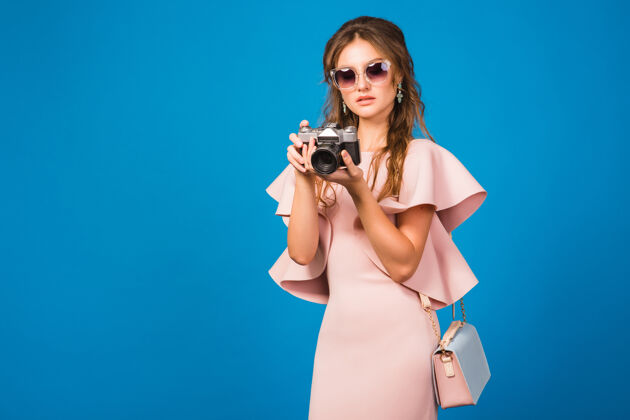 购买穿着粉色奢华连衣裙的年轻时尚女士在老式相机上拍照人夏天漂亮