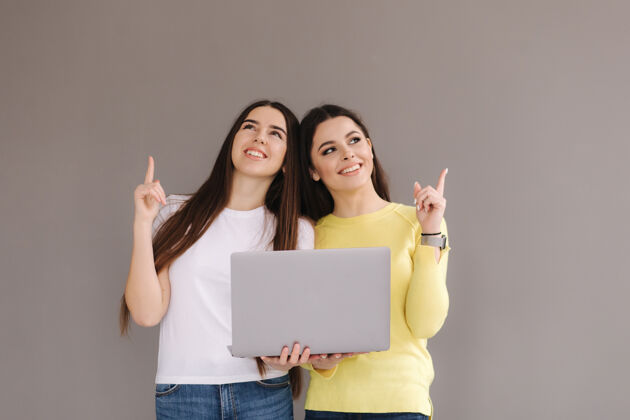 微笑两个女人抱一个laptop.females拿起手指 微笑迷人女人站着手