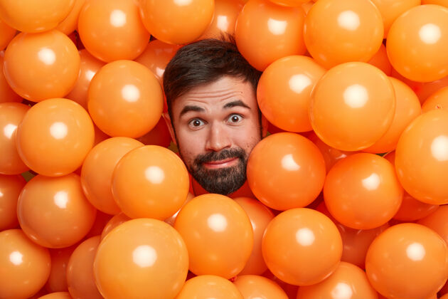 氦一位留着胡须的成年欧洲男子的头像被充气的橙色气球包围 准备参加派对惊喜惊艳年轻
