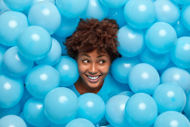 脸卷发女人从充气的蓝色气球中探出头来 笑容灿烂 心情愉快 庆祝什么高兴人面部