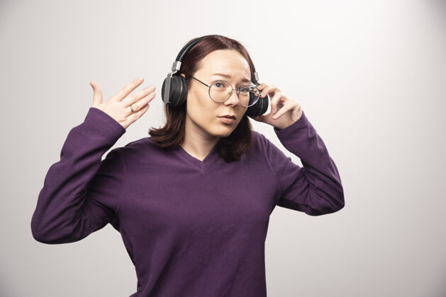 人类戴着眼镜的年轻女子戴着耳机在听音乐 这是一张高质量的白色照片耳机青春眼镜