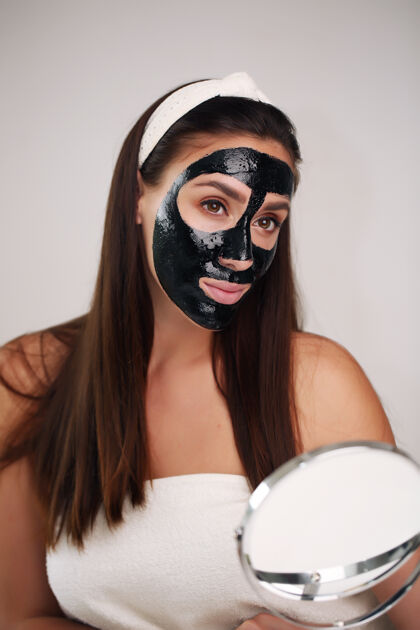 治疗一个戴着洁面黑面具的年轻漂亮女人的画像美容皮肤护理粘土