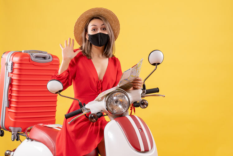 旅游正面图：戴着黑色面具的年轻女士拿着地图挥手靠近轻便摩托车人摩托车车辆