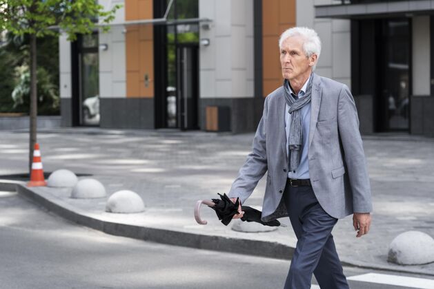 老年人时髦的老男人在城市里一边撑着伞过马路成熟老年人步行