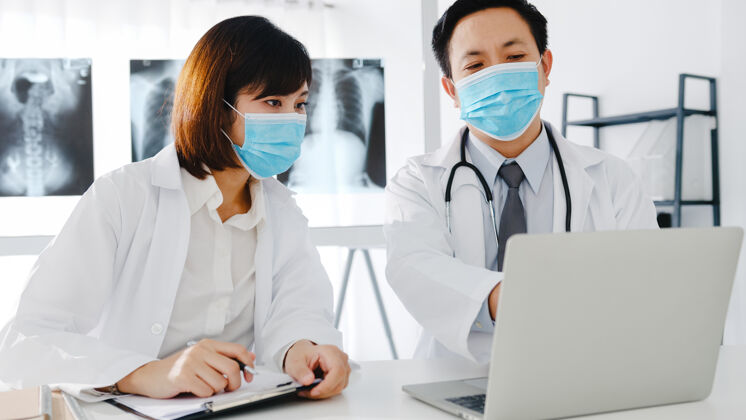 护理亚洲医疗队的男青年女医生戴着防护面罩在医院办公室讨论电脑断层扫描结果员工专业手术