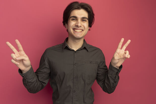 男人面带微笑的年轻帅哥穿着黑色t恤 在粉红色的墙上显示出和平的姿态年轻帅哥姿势