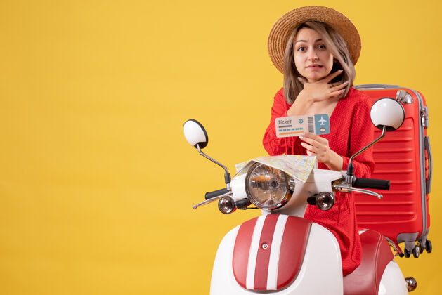 人正面图：穿着红裙子的年轻女士拿着车票 用轻便摩托车捂着喉咙喉咙手提箱旅游