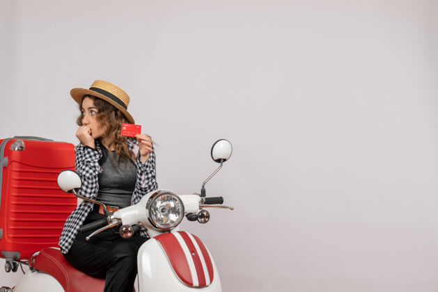左前视图：骑着轻便摩托车的年轻女子拿着卡片看着左边摩托车年轻女子手提箱