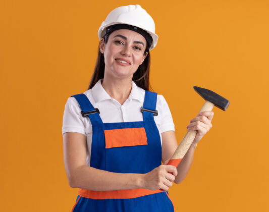 衣服身着制服的年轻建筑工人高兴地把锤子孤立在橙色的墙上年轻人女人请
