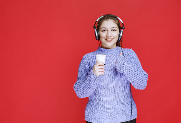成人戴着耳机的女孩拿着咖啡杯 展示着享受的标志Dj品味员工