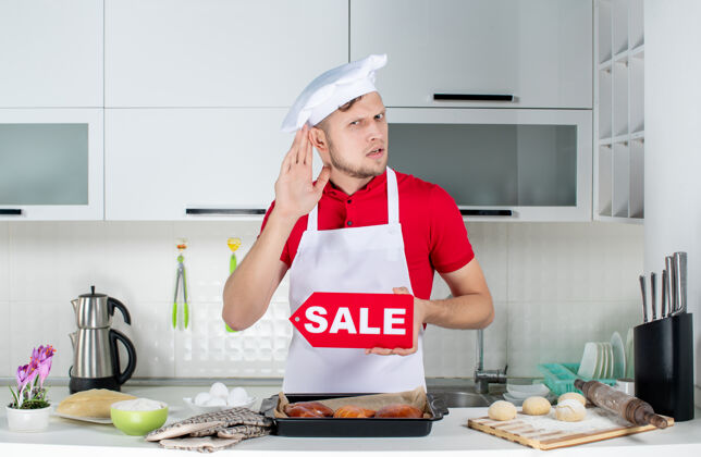 男厨师年轻的男厨师在白色厨房里展示销售招牌 听拉丝闲聊的俯视图围裙房子食物
